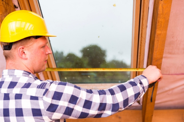 handyman taking measurements in the attic to know the right attic air conditioner size