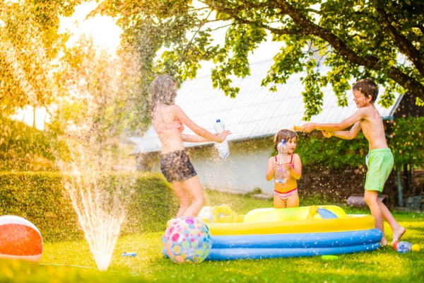 3 kids playing and having fun with inflatable pool and fountain to keep cool in summer