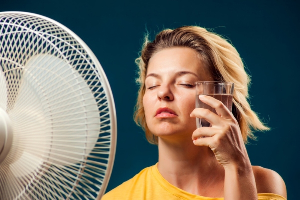 woman experiencing heat exhaustion during summer with glass of water on face in front of fan