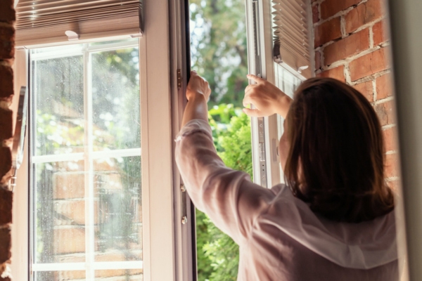 woman opening window to let cool air in during summer