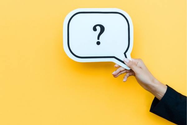 woman's hand against a yellow background holding a question mark sign depicting FAQs