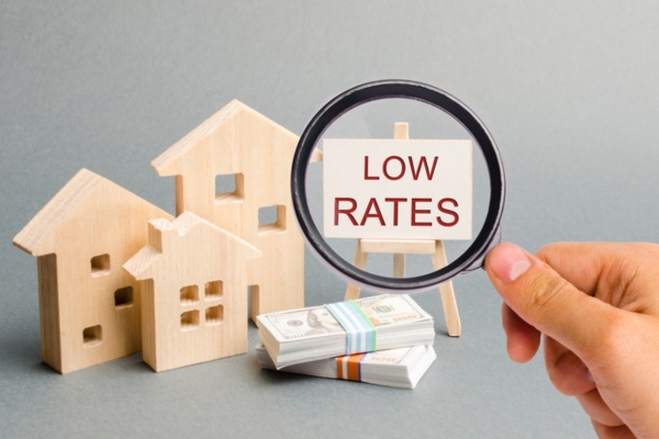 Magnifying glass looking at a poster with the words Low rates beside miniature houses & bundles of money depicting low insurance costs